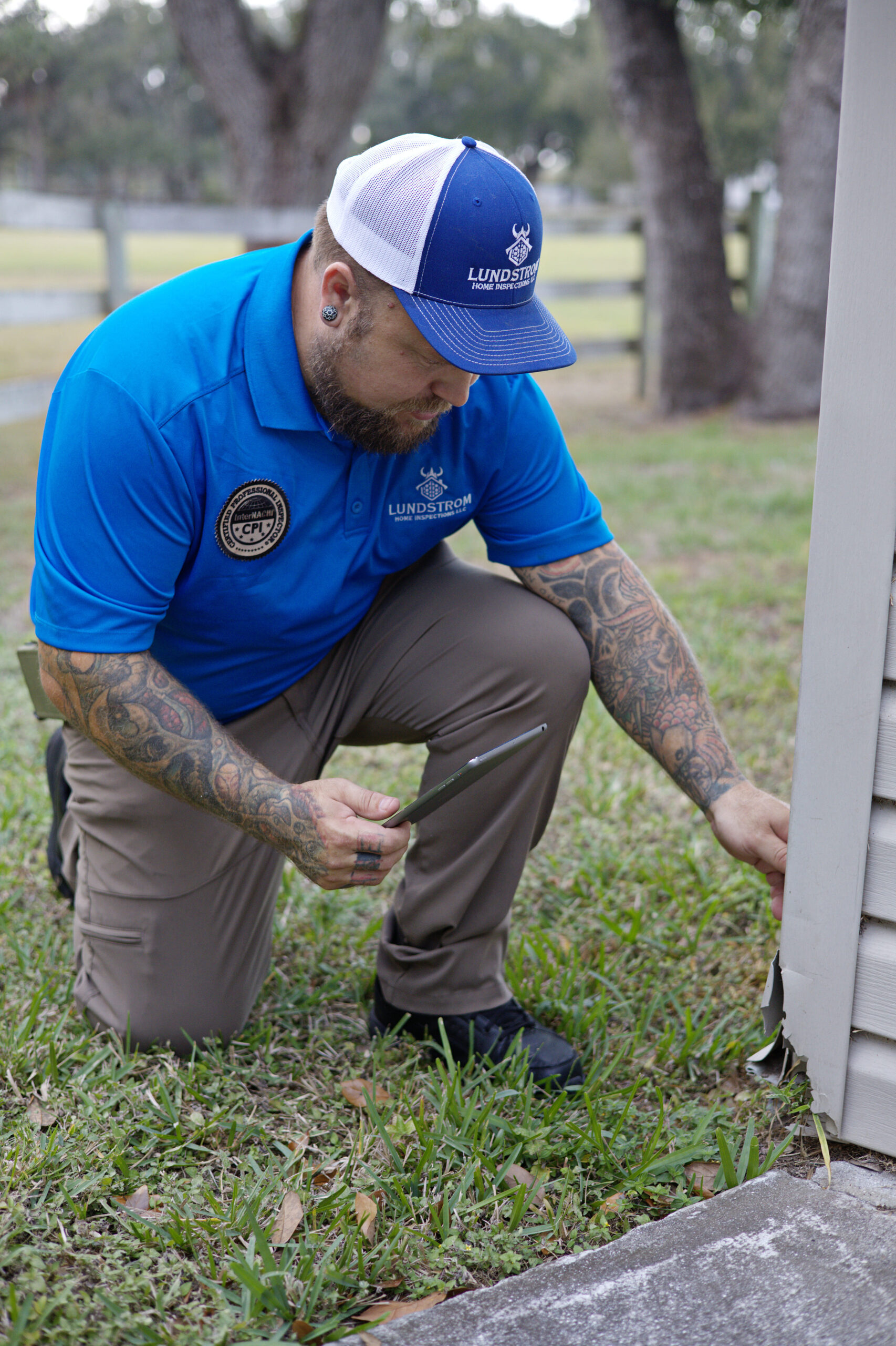 Structural inspection by Lundstrom Home Inspections showing a certified inspector examining exterior wall framing and foundation transition at a residential property.