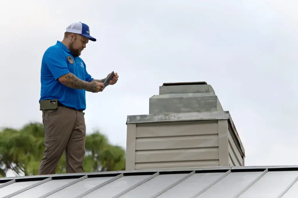 Home inspector using a tablet on a metal roof next to a chimney